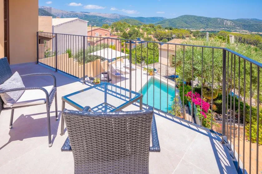 Una zona de estar en un balcón da a una piscina y colinas verdes.