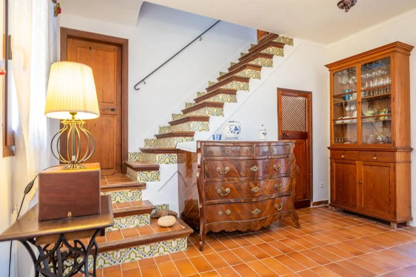 Interior amueblado con una escalera de baldosas, una cómoda de madera y un armario con puertas de vidrio.