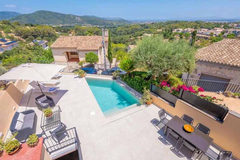 Una zona de piscina al aire libre con asientos de patio y vegetación mira hacia un paisaje de colinas.