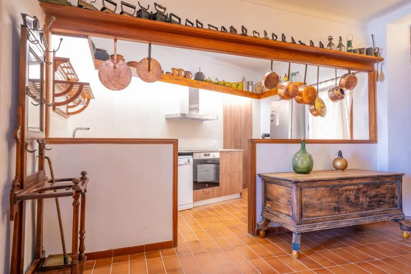 Una cocina con muebles de madera y utensilios de cobre colgados de una viga.