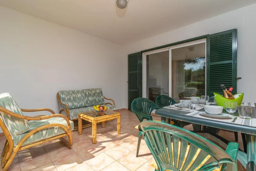 A patio dining area with green seating and a glass-top table beside sliding doors.