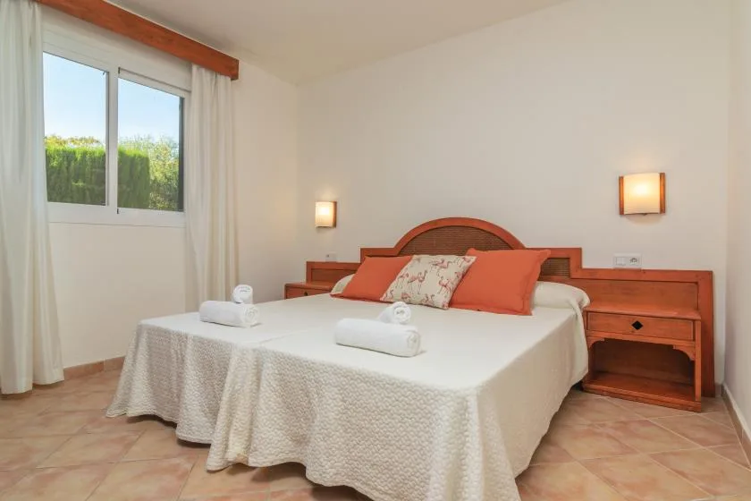 A bedroom with a double bed, white bedding, and a window overlooking greenery.