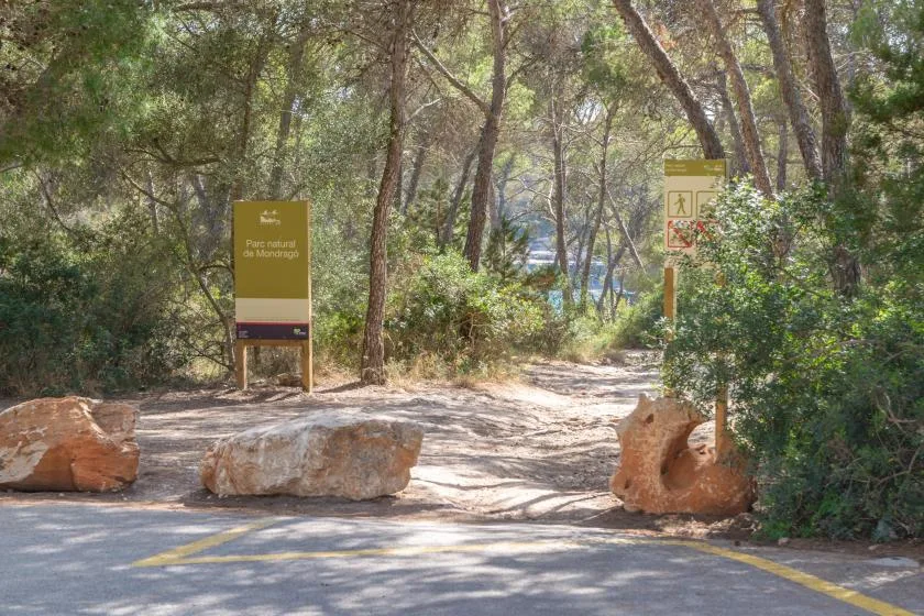 A wooded path entrance is marked by signs and large rocks.