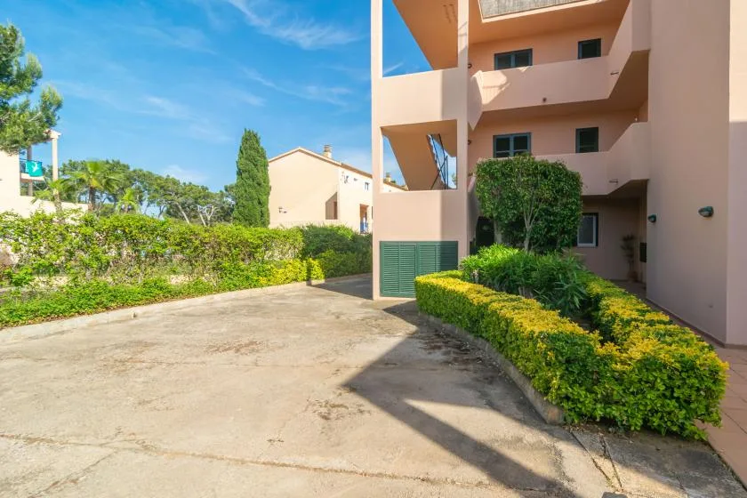 A paved courtyard beside a peach-colored building, with low green hedges along the walkway.