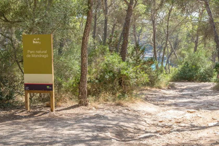 A shaded dirt path winds through trees beside a park sign.