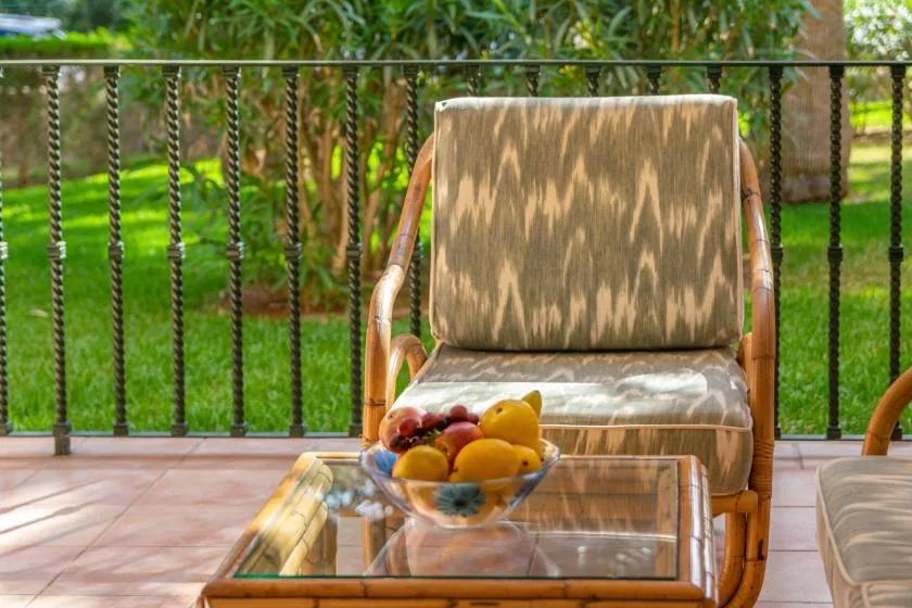 A patio seating area with a glass table and a bowl of fruit.