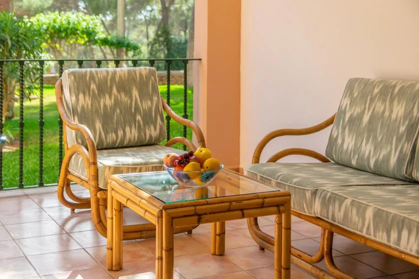 A seating area with a glass-top table and fruit bowl beside a garden view.