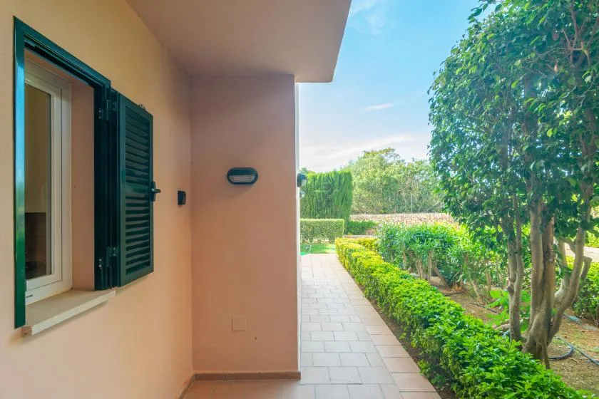 A tiled walkway runs beside a peach-colored building and green hedges.