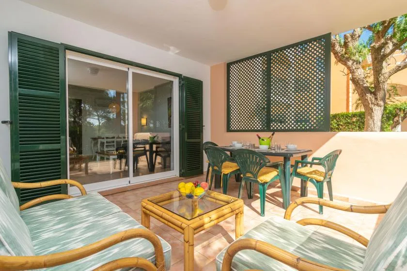 A sunny outdoor patio with seating around a table beside sliding glass doors.