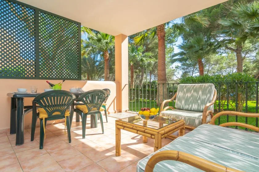 Un patio cubierto tiene una mesa de comedor y asientos al aire libre, rodeados de vegetación.