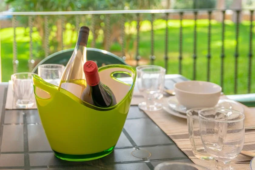 Una mesa está preparada con vasos, platos y una hielera verde para vino.
