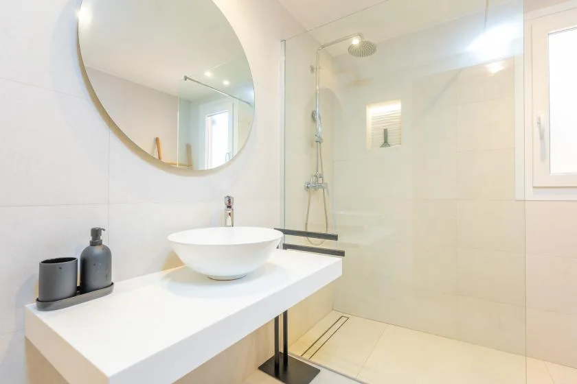 A bright bathroom with a vessel sink, round mirror, and glass shower.