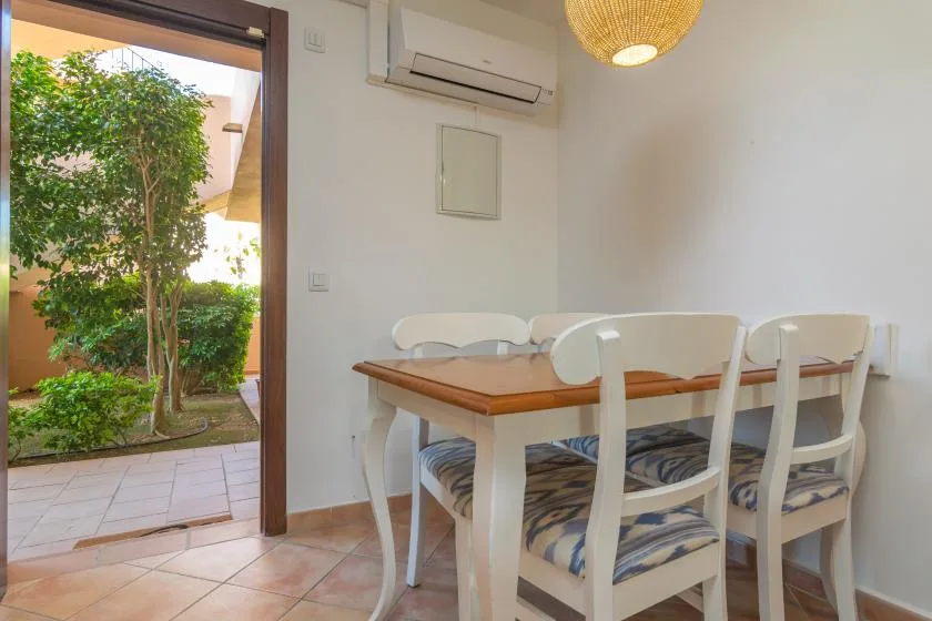 A dining area with a wooden table and white seating beside an open patio doorway.