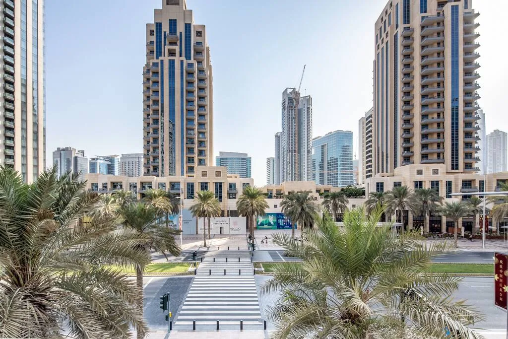 A city plaza with palm trees and modern high-rise buildings.