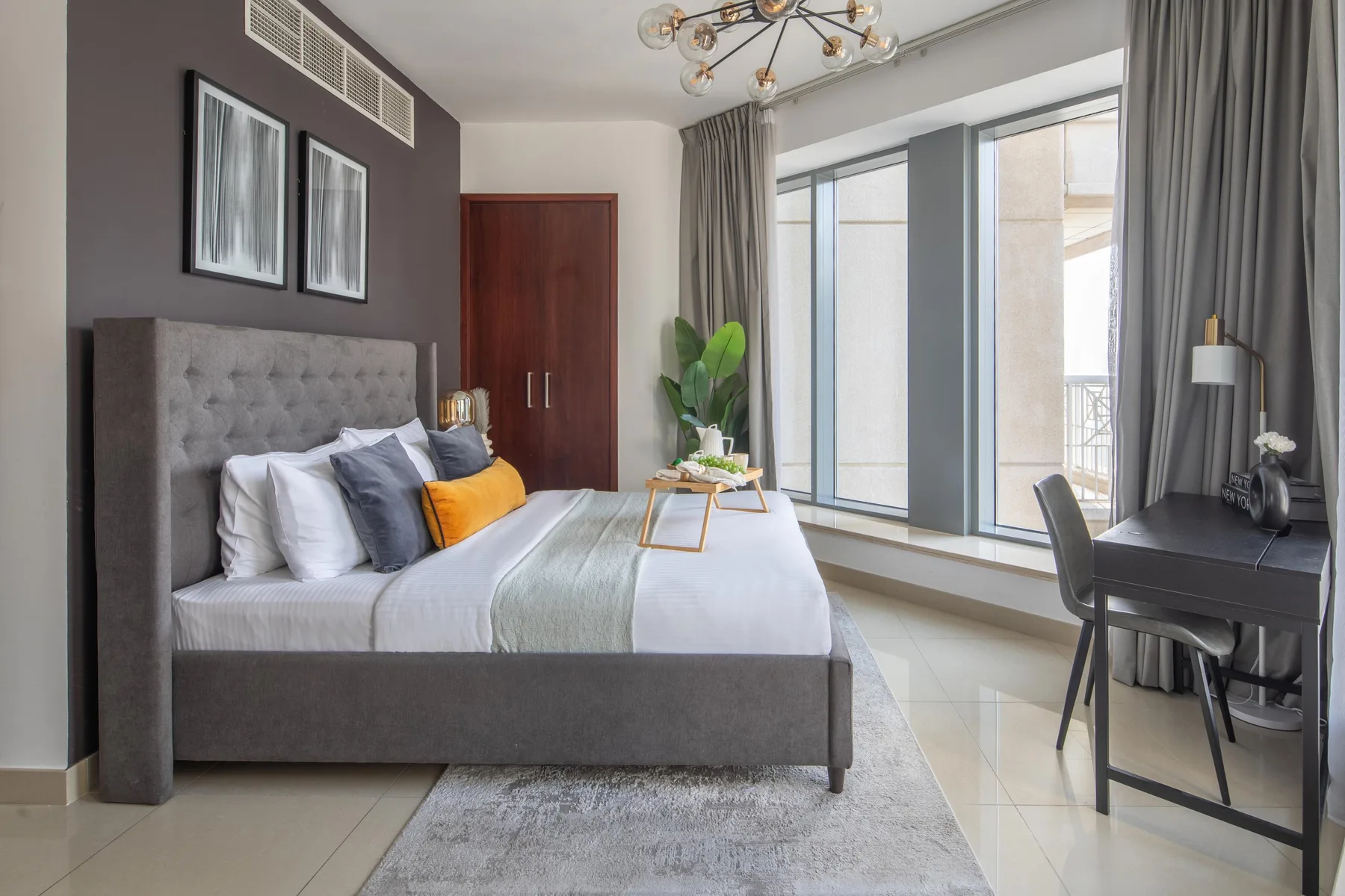 A bedroom with a neatly made bed beside large windows and a desk.