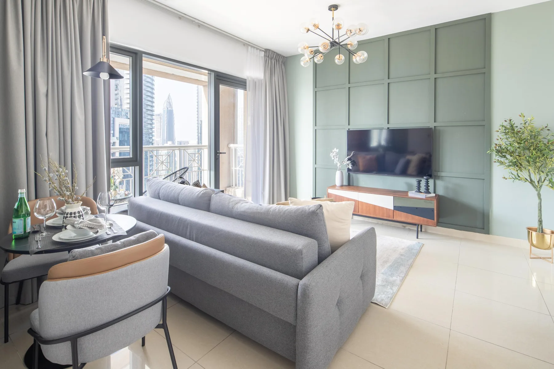 A bright living room with gray seating, a television, and large windows.