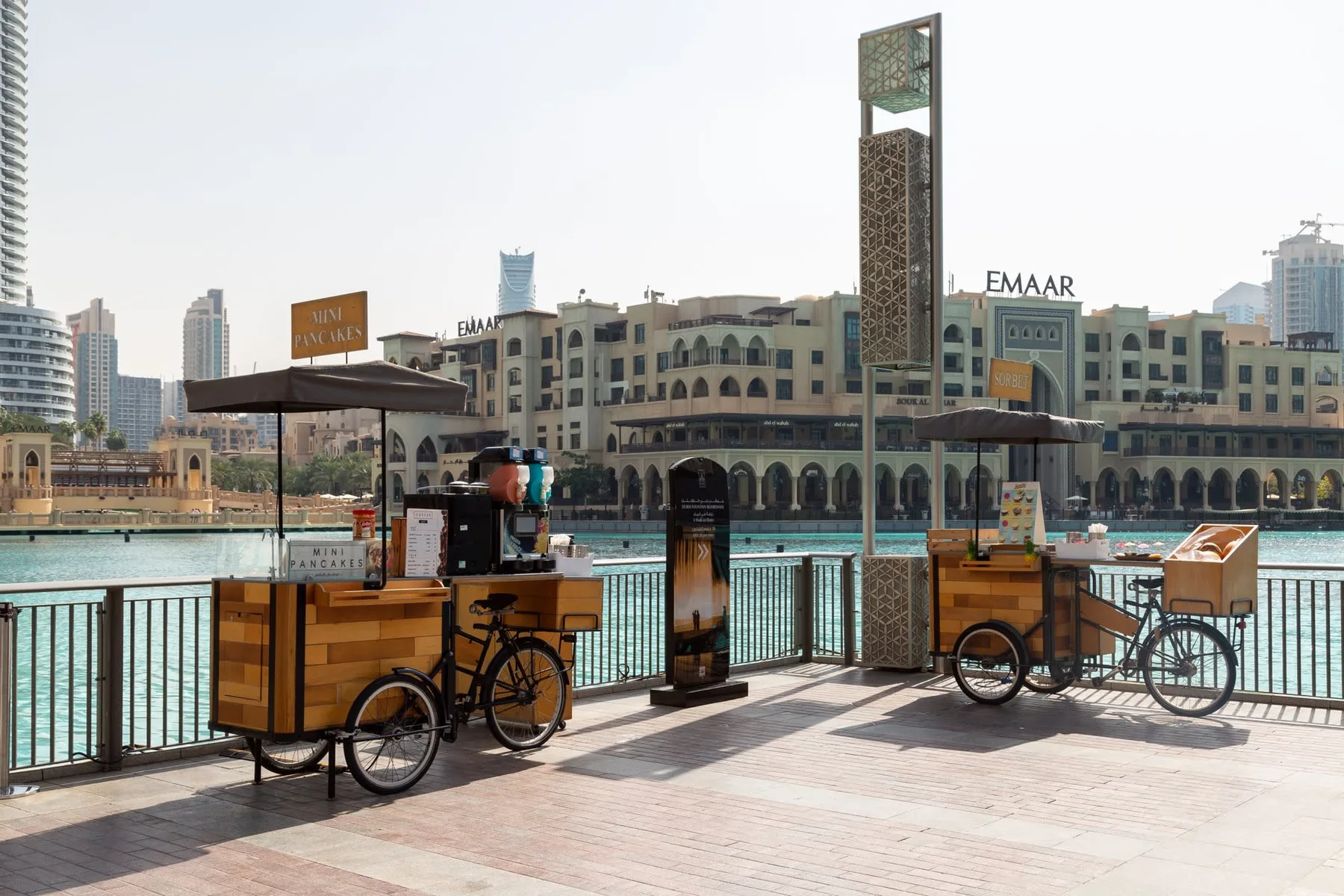 Outdoor waterside promenade with two wooden food carts beside a railing.