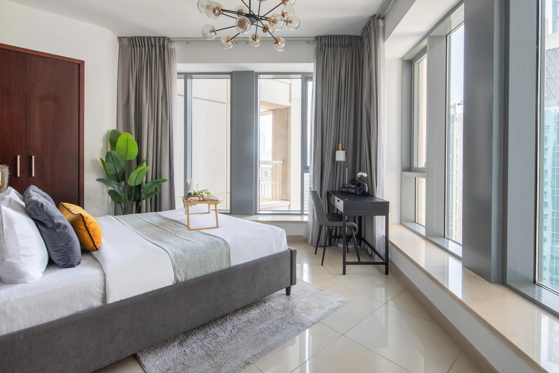 A bright bedroom with a bed, desk, and floor-to-ceiling windows.