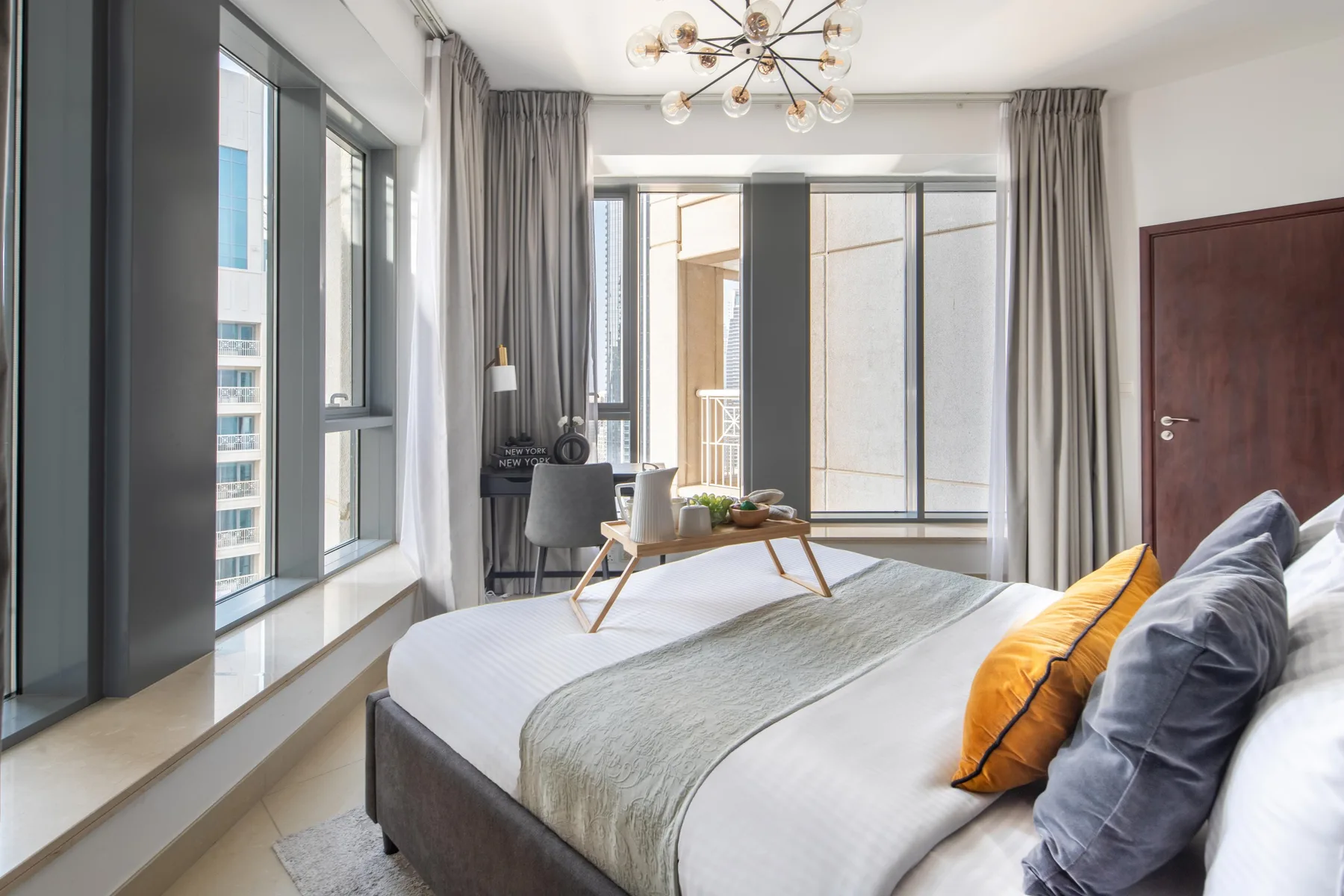 A bright bedroom with a bed beside tall windows and gray curtains.