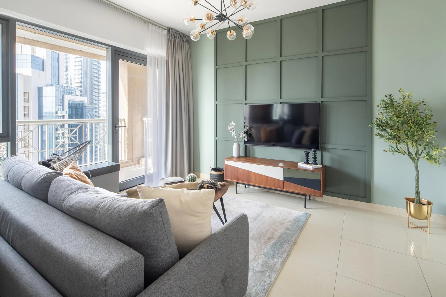 A living room with a gray sofa facing a television on a green paneled wall.