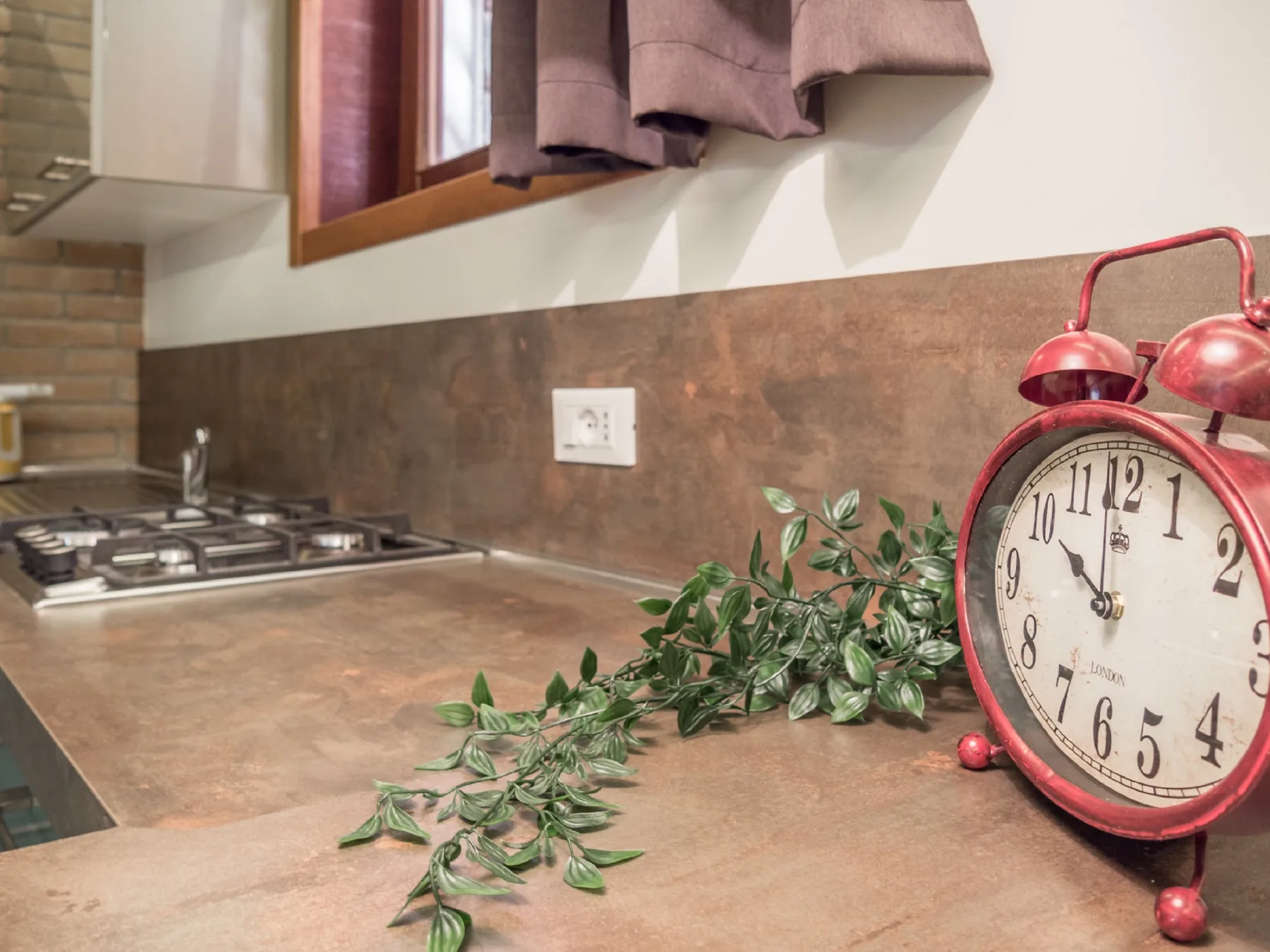 Una encimera de cocina con una estufa de gas, una planta colgante y un reloj rojo.