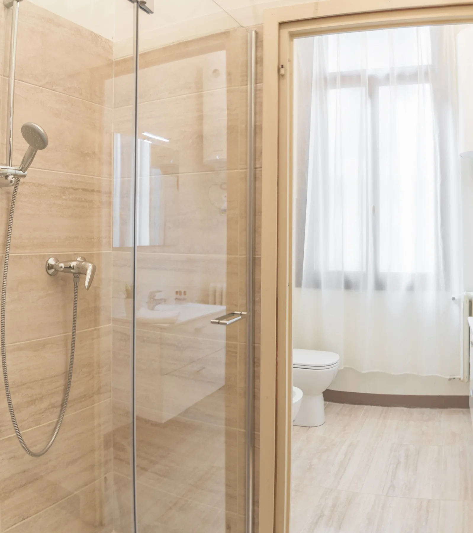 Un baño alicatado con ducha de vidrio y una ventana con cortina.