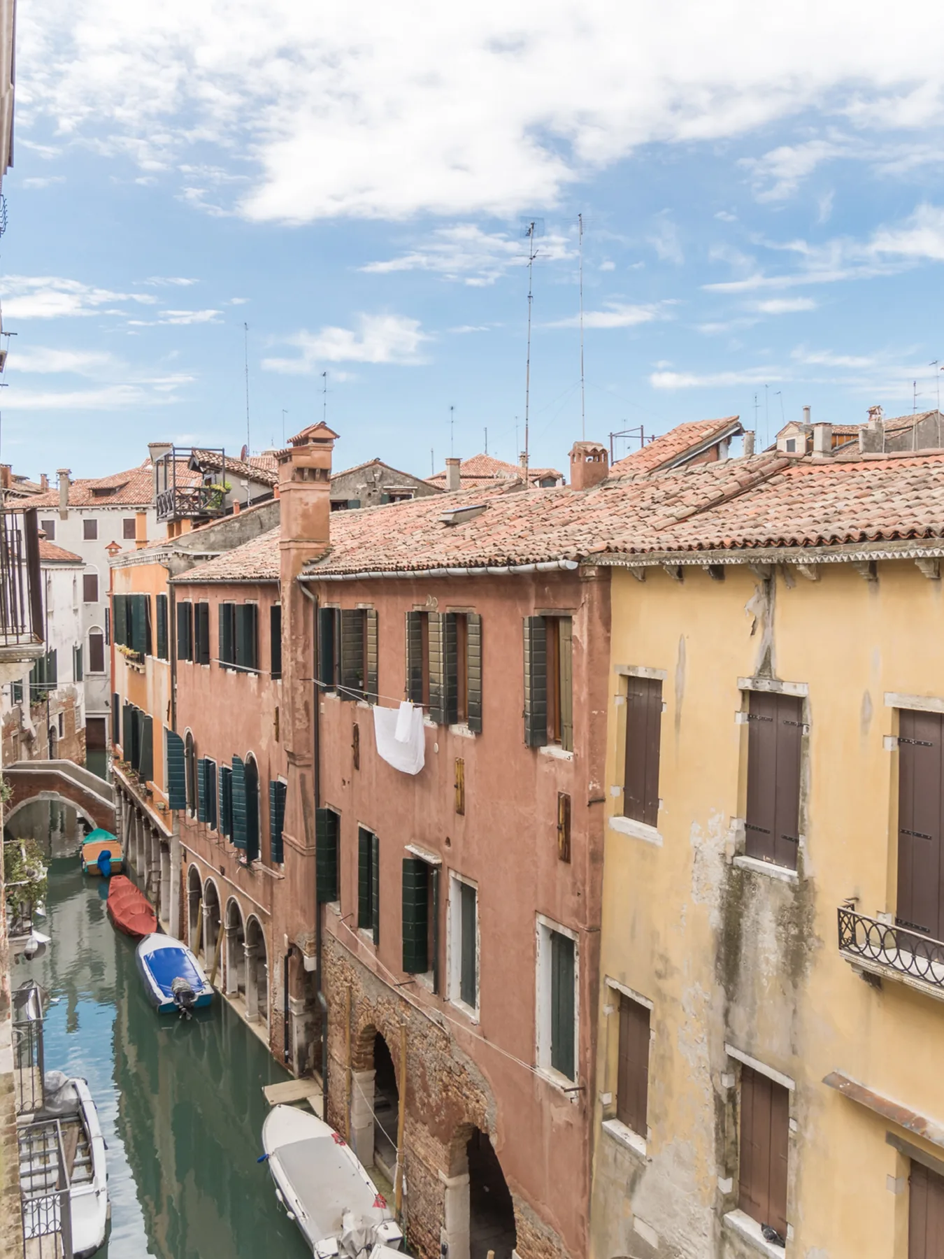 Un canal estrecho pasa entre edificios de colores con tejados de terracota bajo un cielo parcialmente nublado.