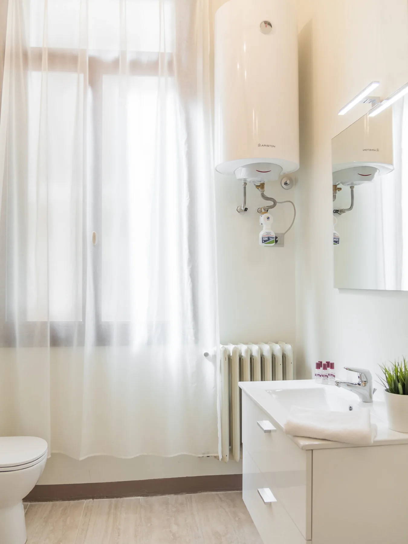 Un baño luminoso con lavabo, espejo de pared y cortinas translúcidas.