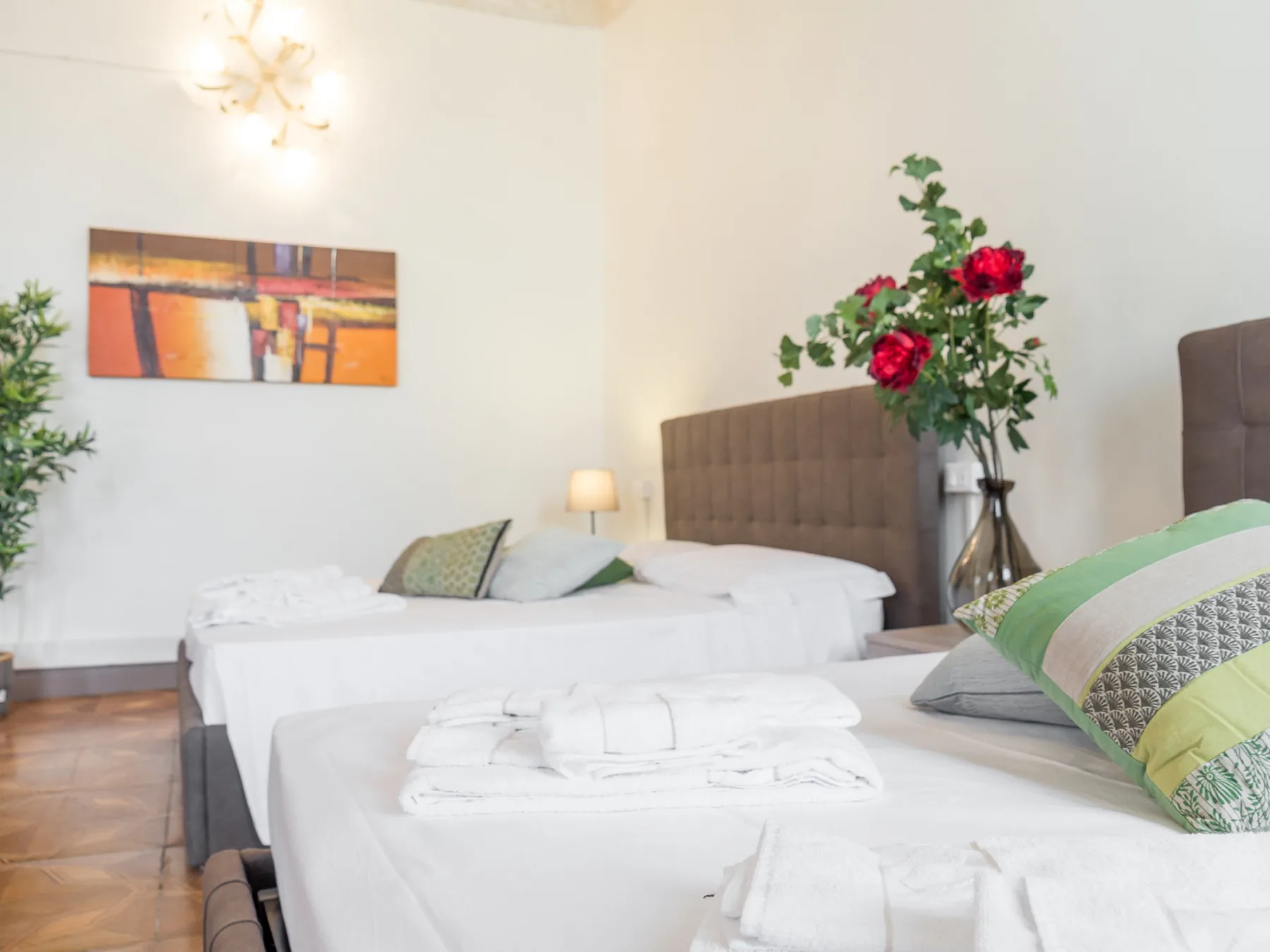 Un dormitorio luminoso con camas blancas, cabeceros tapizados y un jarrón con flores.