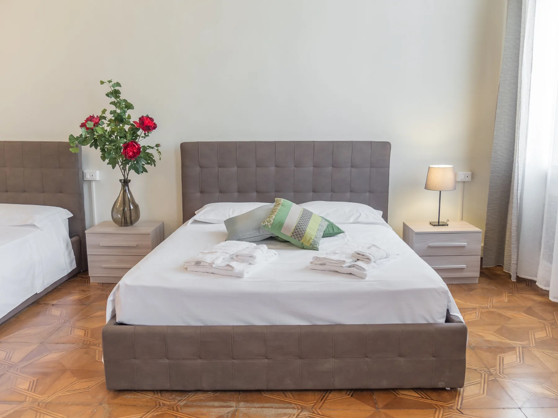 Un dormitorio con una cama bien tendida, mesitas de noche y flores.