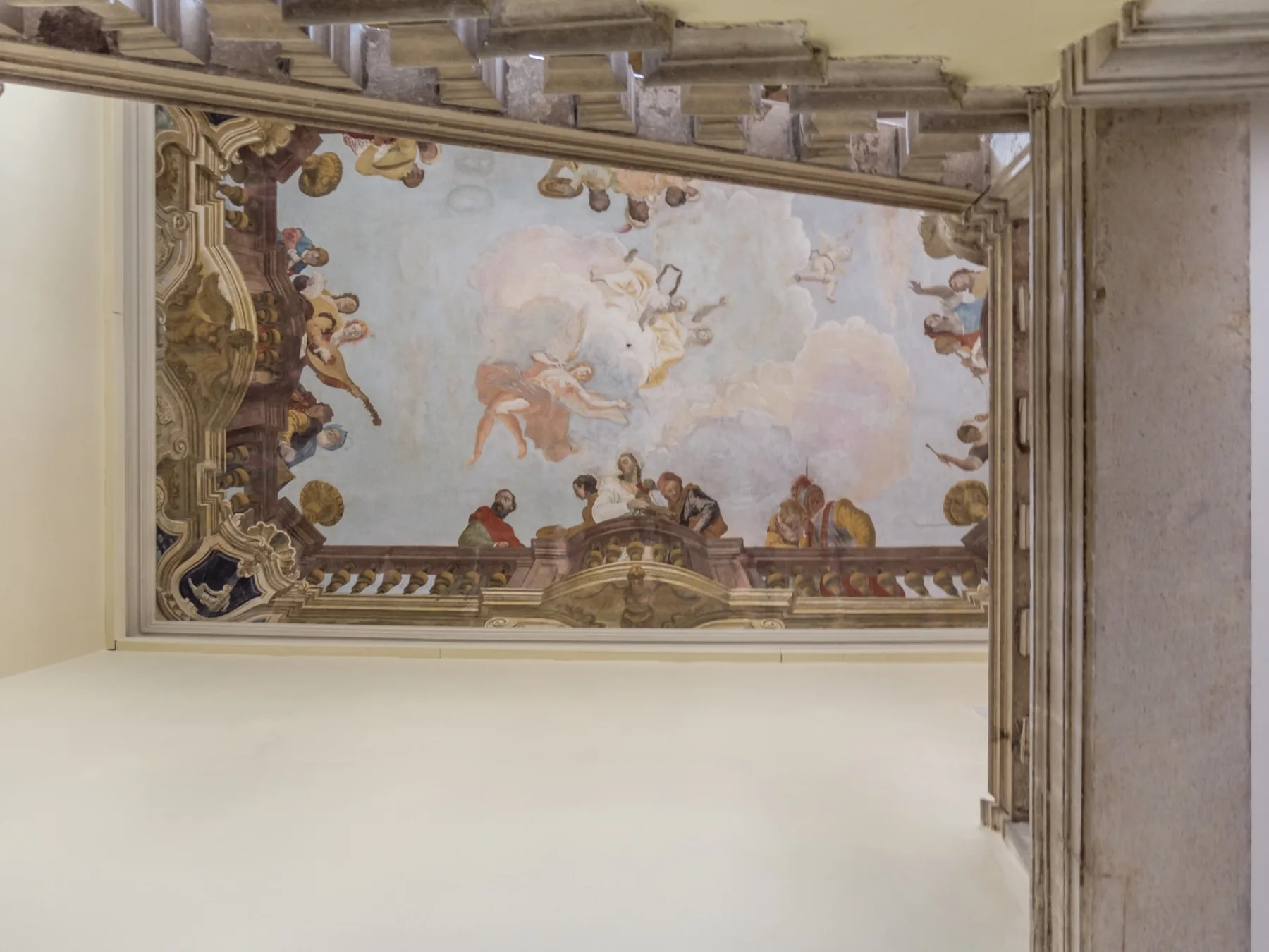 Un fresco ornamentado en el techo con figuras pintadas y bordes arquitectónicos decorativos.
