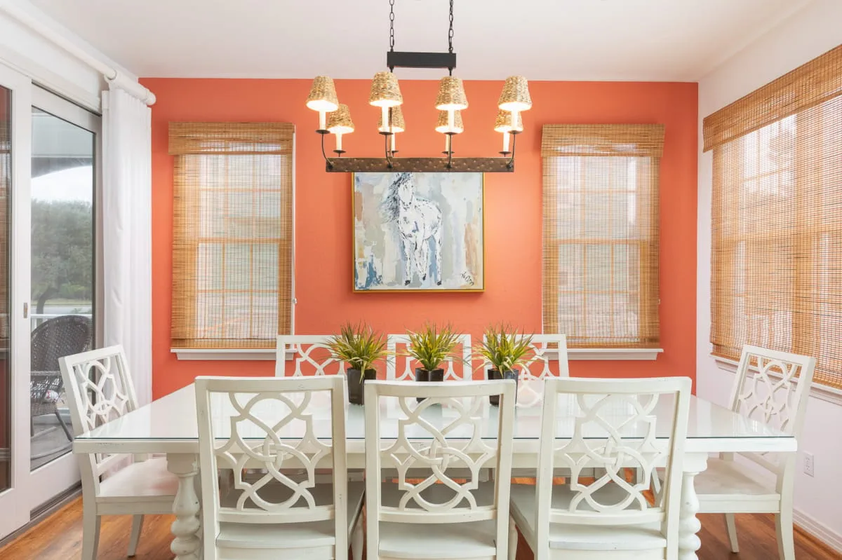 Un comedor luminoso con una mesa larga, asientos blancos y una pared coral.