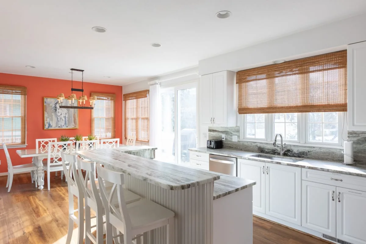 Una cocina luminosa con una isla larga y asientos blancos junto al comedor.