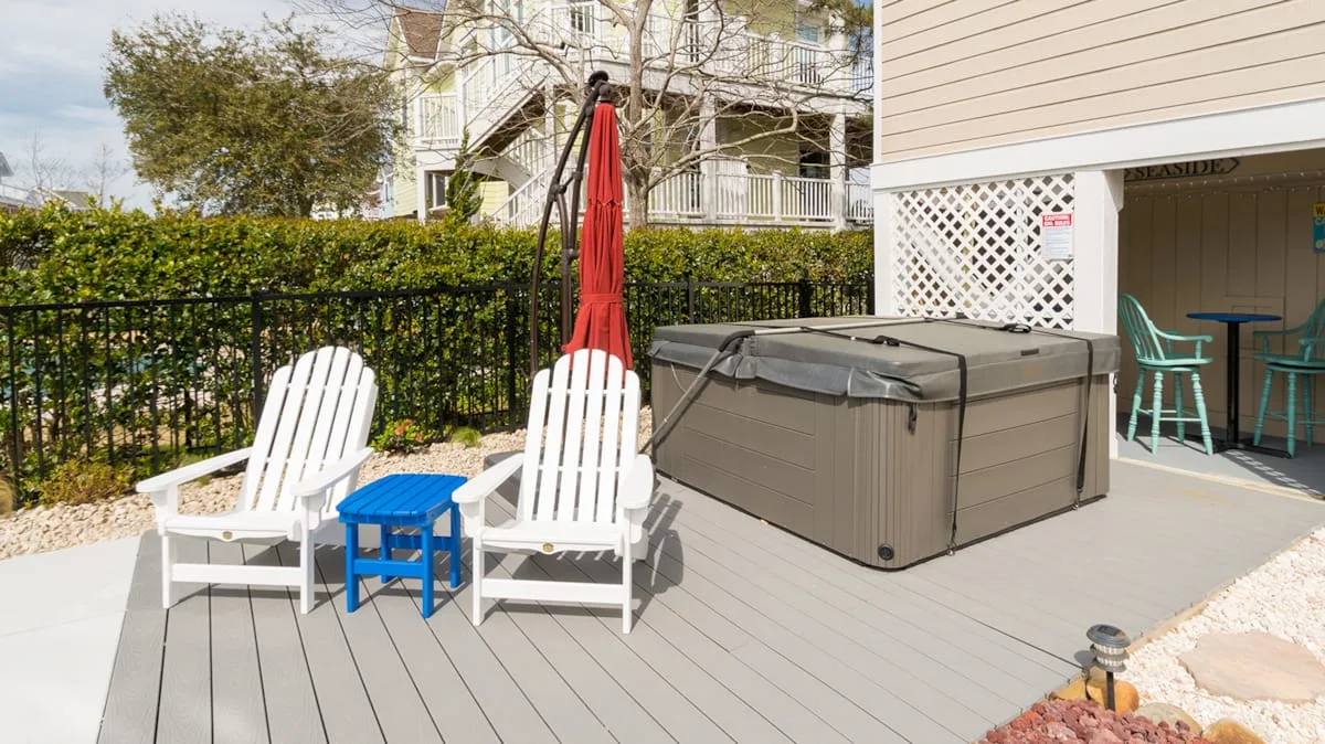 An outdoor deck with a covered hot tub, white seating, and a red umbrella.