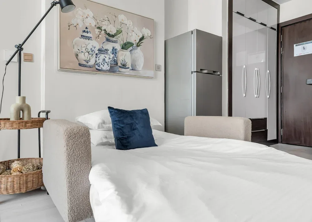 Un dormitorio luminoso con una cama hecha y una pintura floral en la pared.