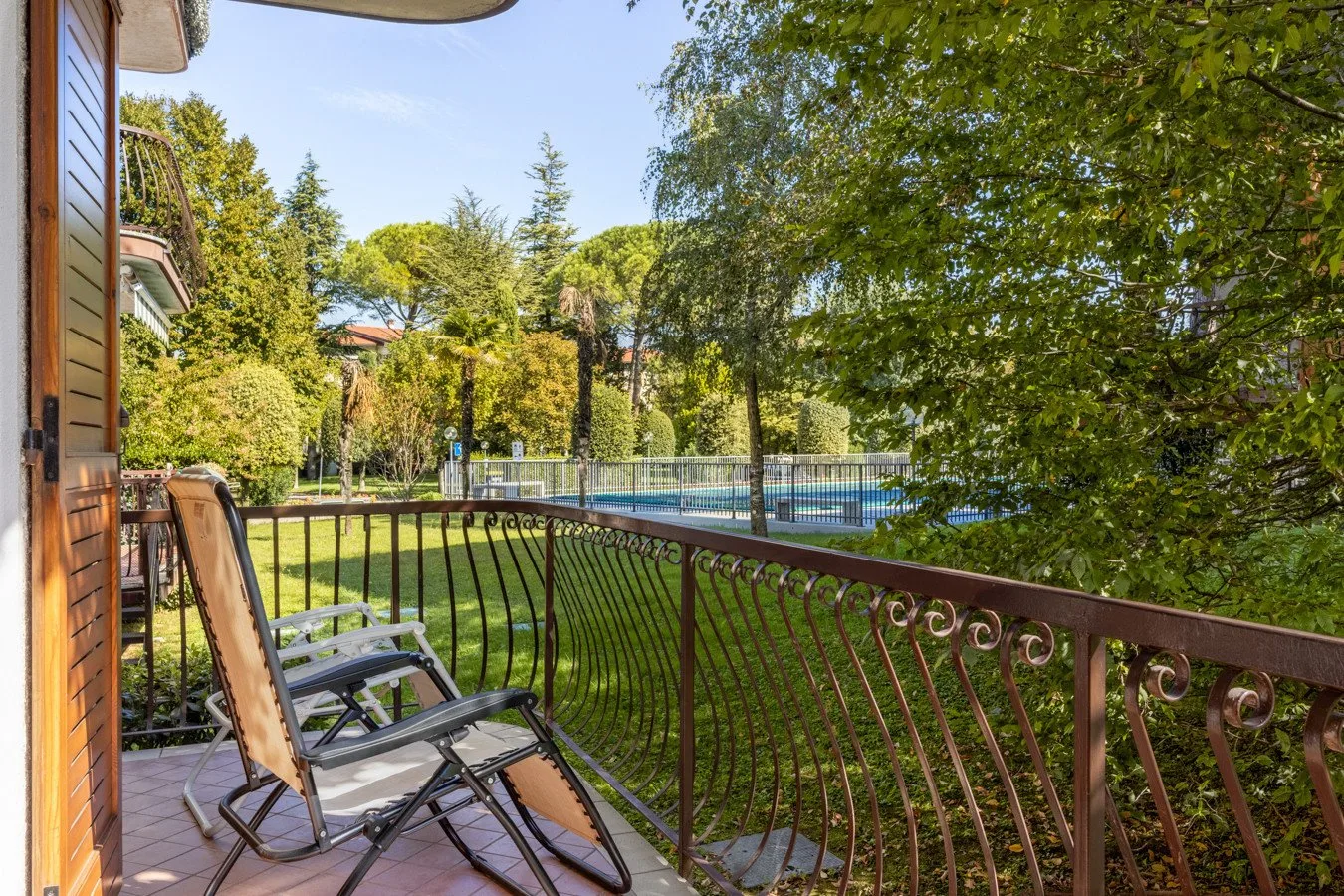Un patio con asientos al aire libre da a un jardín con césped y una piscina.