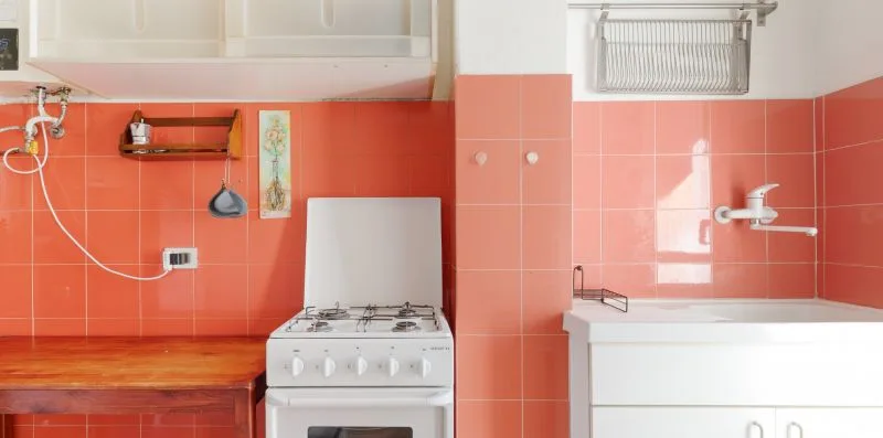 A kitchen with a gas stove, red tiled walls, and white cabinets.