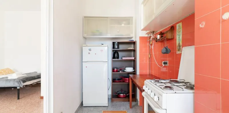 A compact kitchen with a refrigerator, open shelves, and a gas stove.