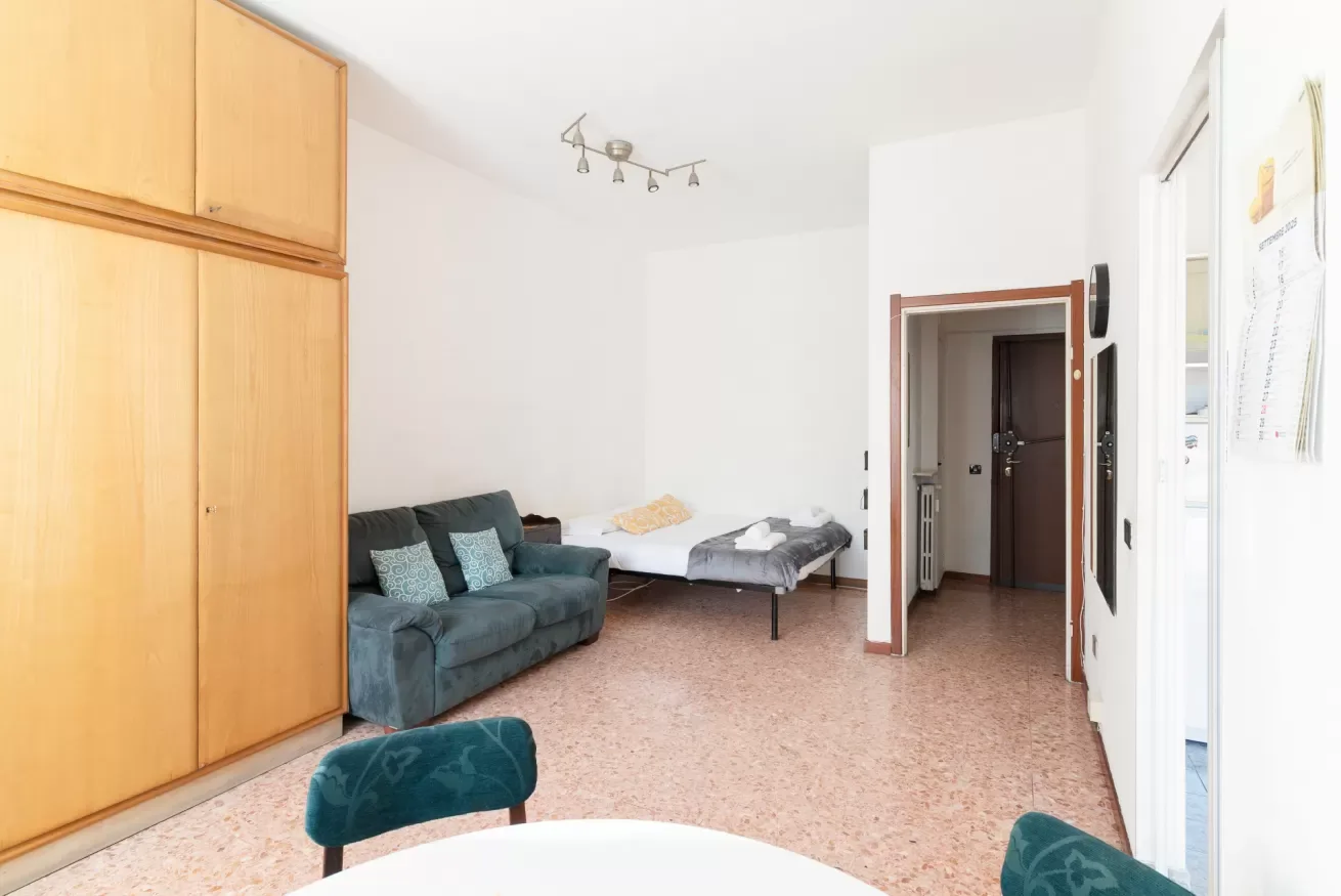 A bright living room with seating and a single bed beside an open doorway.