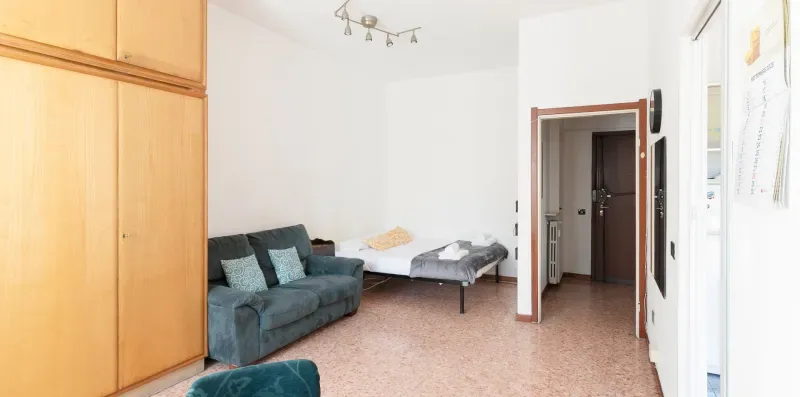 A living room with a teal sofa and a bed beside the doorway.