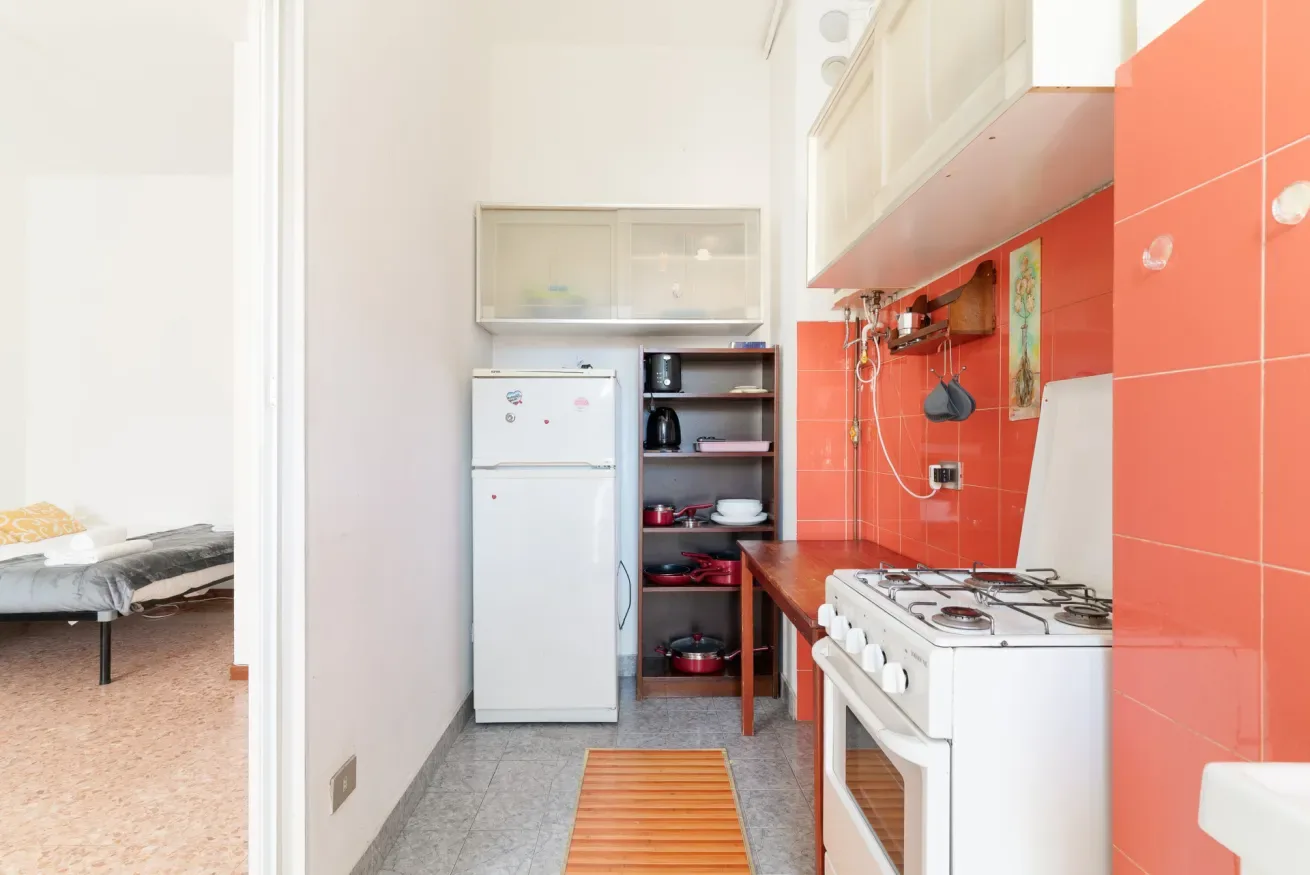 A compact kitchen with red tiled walls, a refrigerator, and a stove.