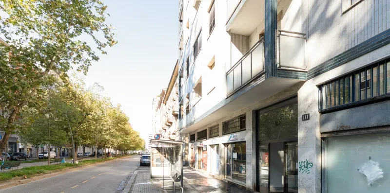 A city street with a modern building frontage and trees along the sidewalk.