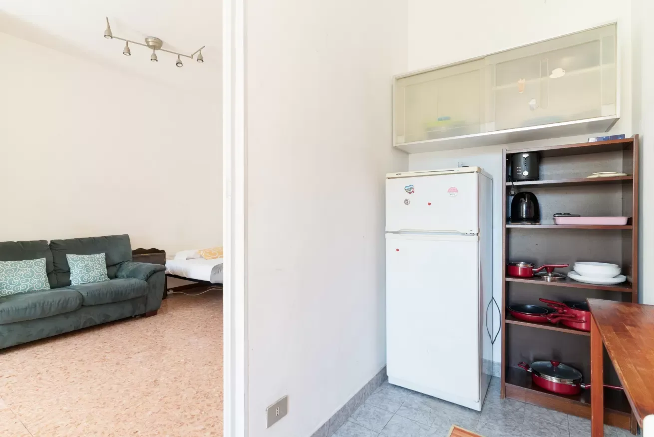 A kitchen area with a refrigerator and open shelving beside a living room.