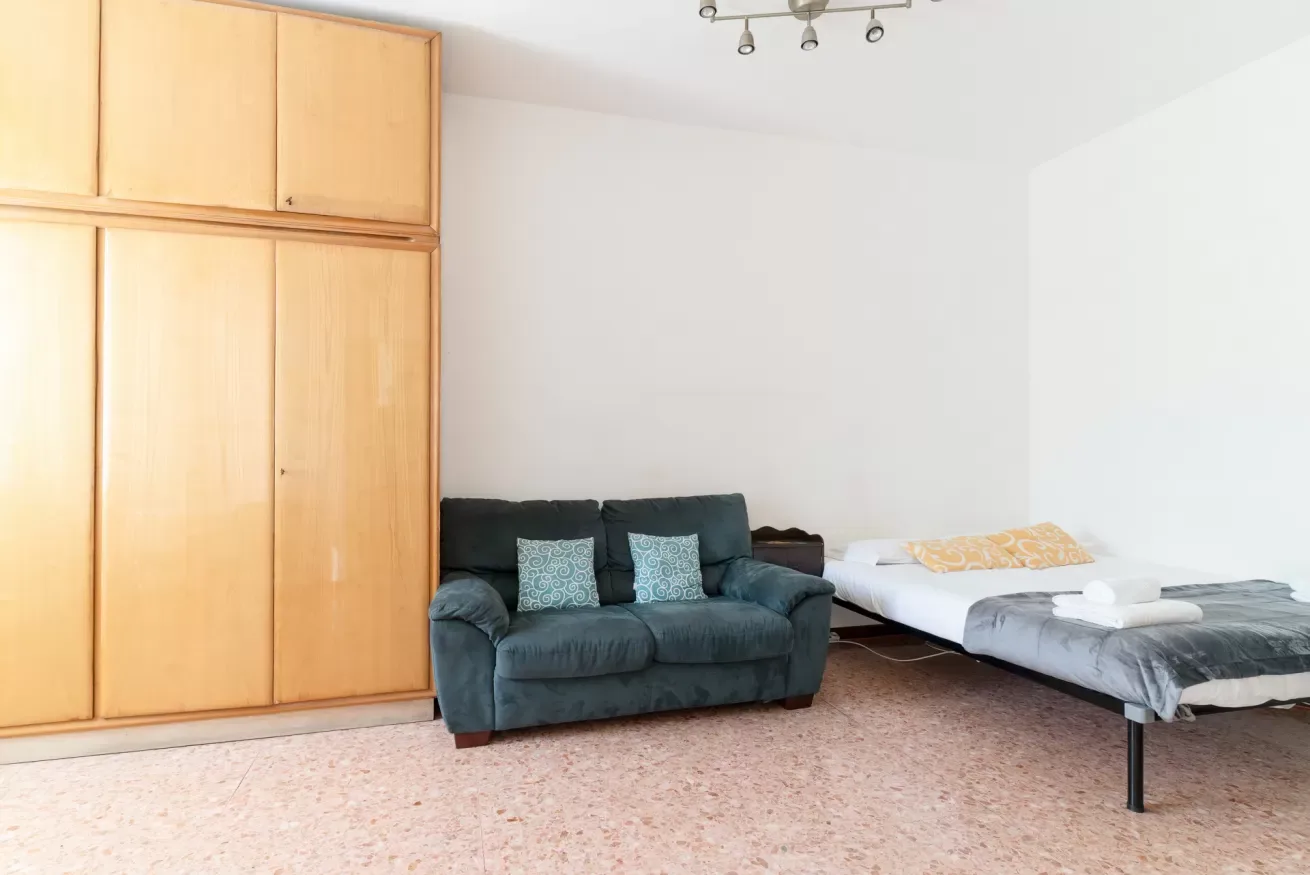 A bedroom with a bed beside a dark seating area and wooden wardrobes.
