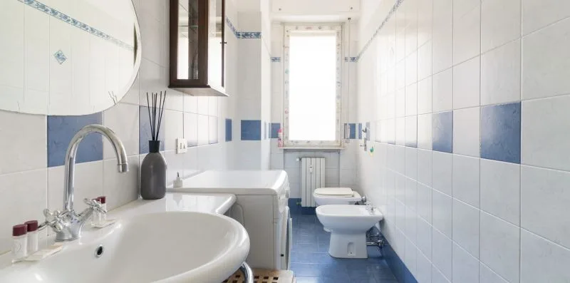 A tiled bathroom with a sink, toilet, and window.