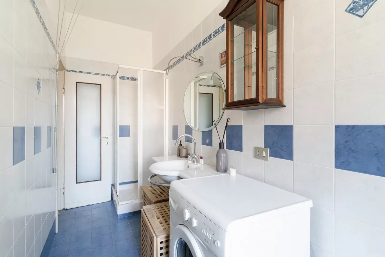 A tiled bathroom with a washing machine, sink, and mirrored cabinet.