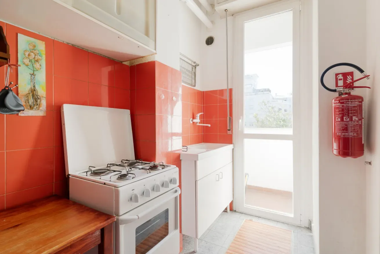 A kitchen with a gas stove, red tiled walls, and a bright glass door.