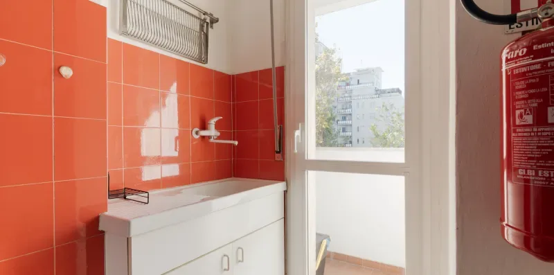A bathroom with a sink beneath a window and orange wall tiles.