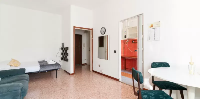 A bright dining area with a white table and green upholstered seating beside a red kitchen.