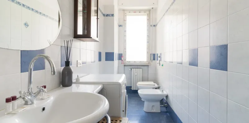 A tiled bathroom with a sink, toilet, and bathtub beside a window.